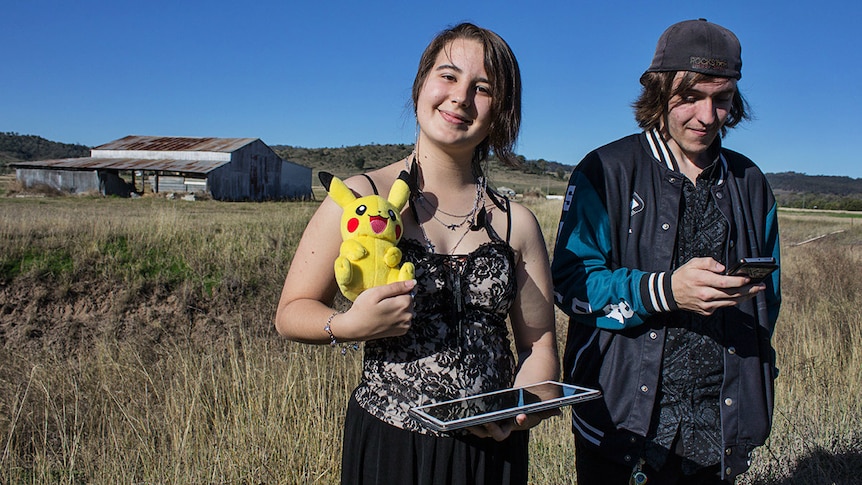 Two people stand in a paddock playing a mobile phone game