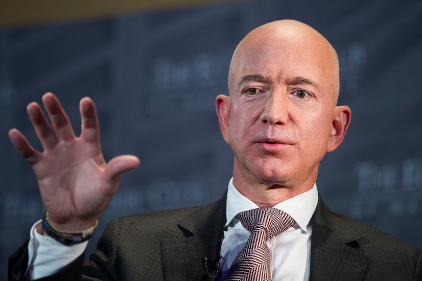 A man in a suit holds his right hand up as he speaks to a crown at an event.