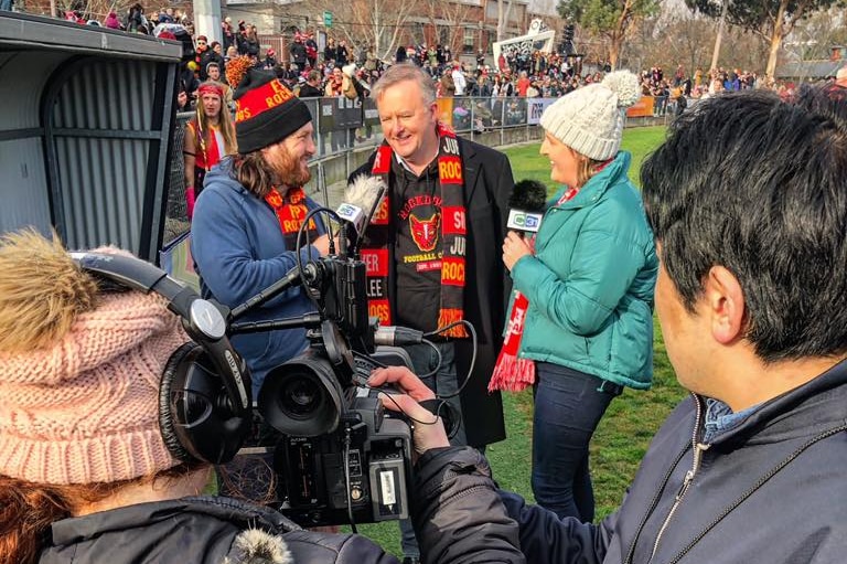 Camera operators look on as two interviewers, a man and a woman with microphones, interview Anthony Albanese.