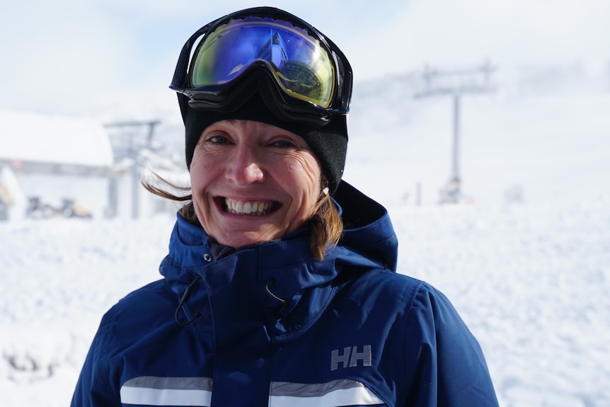 A woman smiling broadly, and wearing ski gear