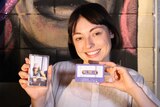 Musician Stella Donnelly sits in front of a mural and holds up a cassette of her new EP