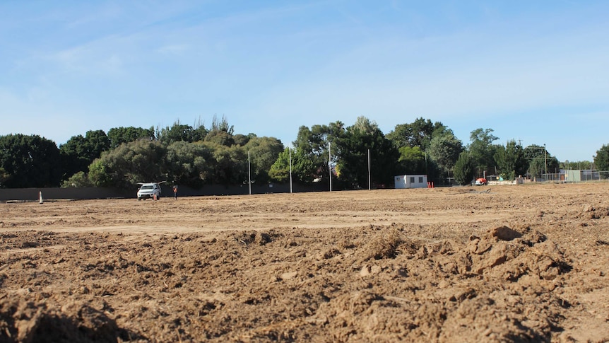 Football posts sit in the background, while the oval is filled with dirt and excavation material.