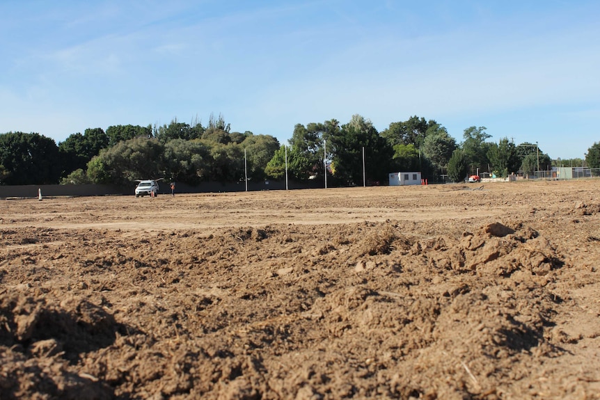 Football posts sit in the background, while the oval is filled with dirt and excavation material.