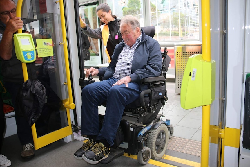 Tom Roper boards a low-rise tram in his wheelchair, with the assistance of a public transport staff member.
