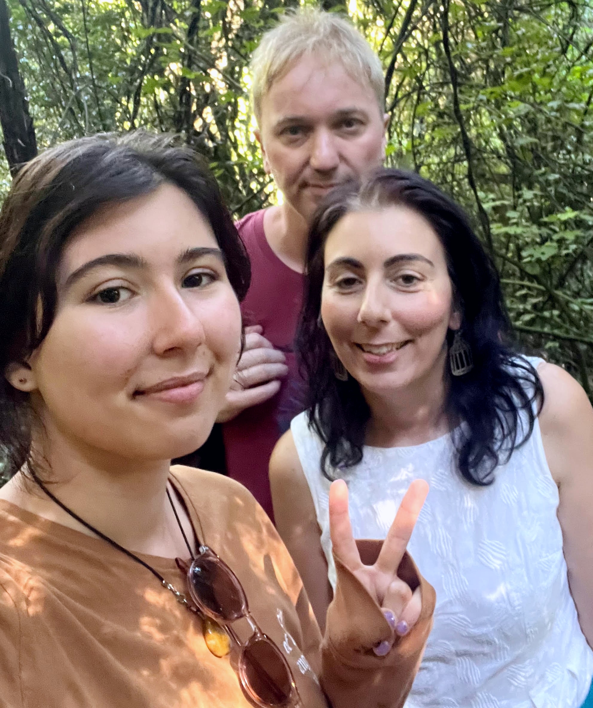 Koraly Dimitriadis stands with her daughter in front and her ex-boyfriend behind in a bushland setting. They are all smiling. 