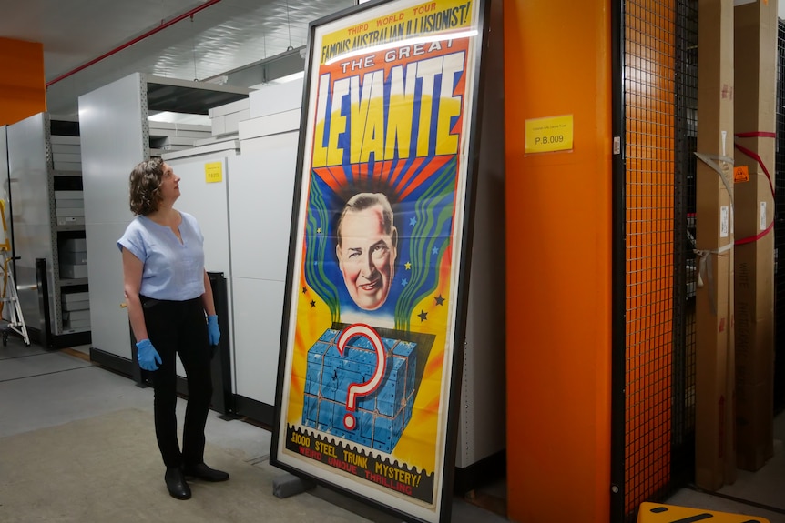 A woman near compactors looks up at a publicity poster that is about a metre taller than her