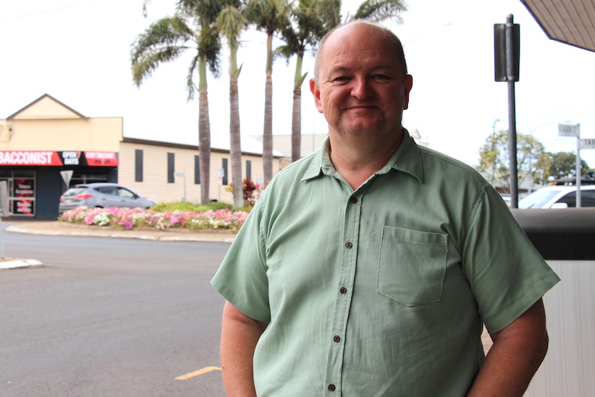 A man in a green shirt smiles at the camera with a roundabout and streetscape behind him