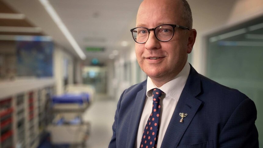 Dr Chris MacIsaac in a hospital corridor smiling at the camera.