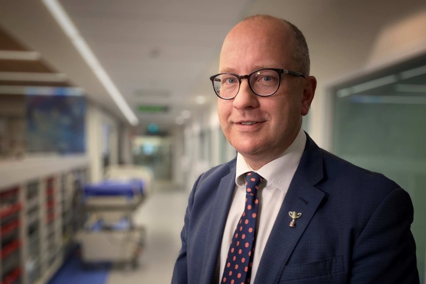 Dr Chris MacIsaac in a hospital corridor smiling at the camera.