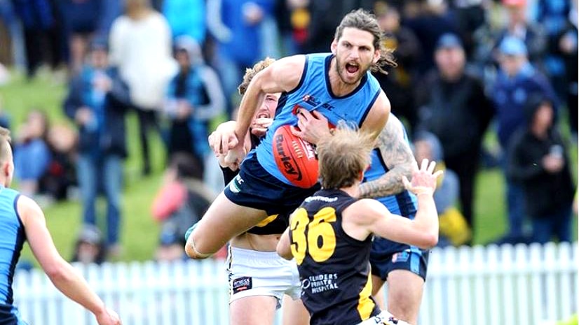 A football player snarls as he lands with the football ahead of an opposition player.