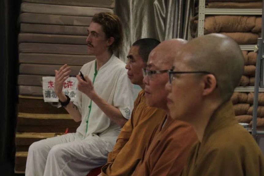 Theo Stapleton translating at a Buddhist studies program in Fujian province He is sitting beside three monks in yellow robes.