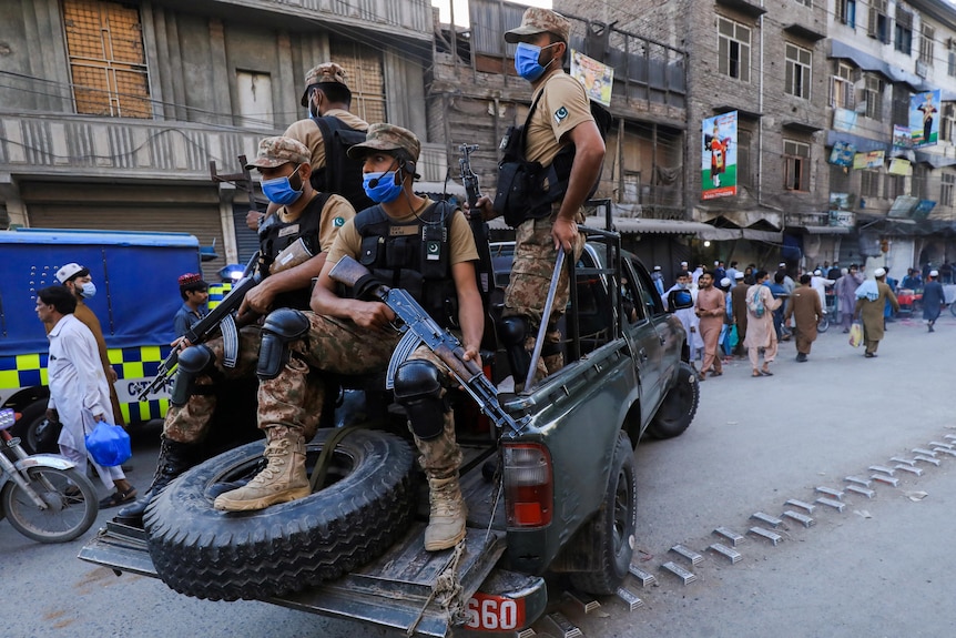 four members of the Pakistani army with guns in the back of the truck patrolling the streets in masks