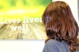 A woman facing away from the camera staring at a wall hanging that says "we believe in lives lived well"