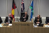 Five people sit behind a long desk at the City of Canada Bay Council with the acting mayor raising his hand while he speaks