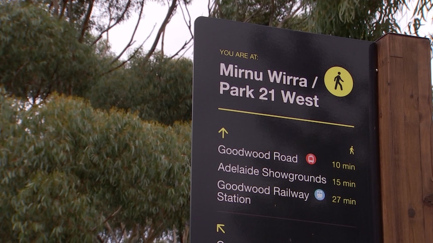 A sign reading 'Mirnu Wirra/Park 21 West' with directions on it, with trees behind it
