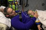 A woman holds her child who is hooked up to an oxygen mask