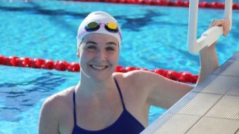 A woman holds onto a block in a swimming pool while looking at the camera.