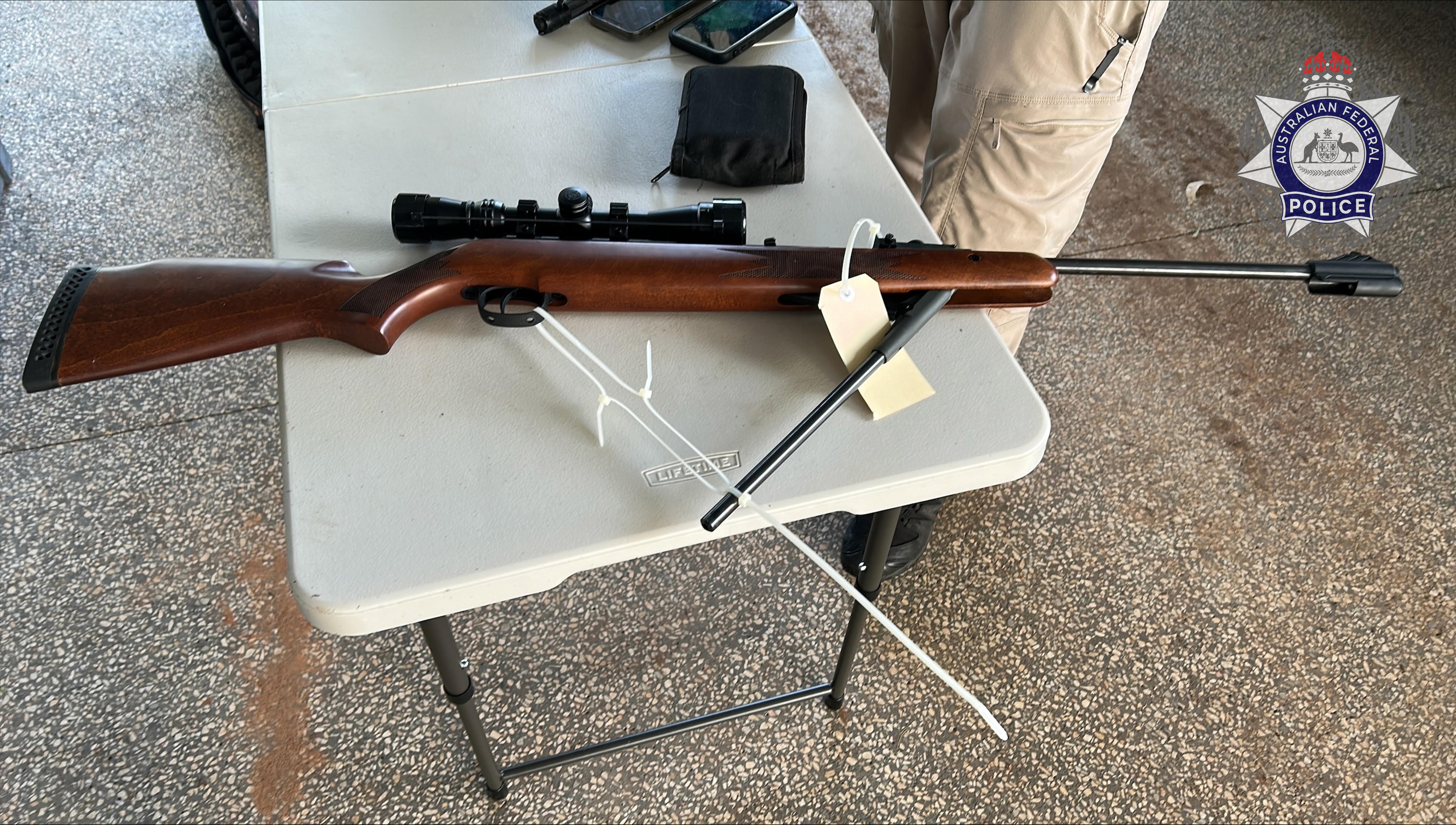 Um rifle marrom sobre uma mesa dobrável branca, com fechos de correr em volta do suporte.