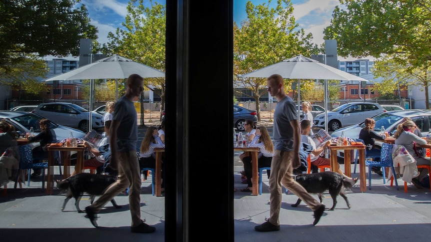 A man walks past cafes and restaurants on a street in Canberra.