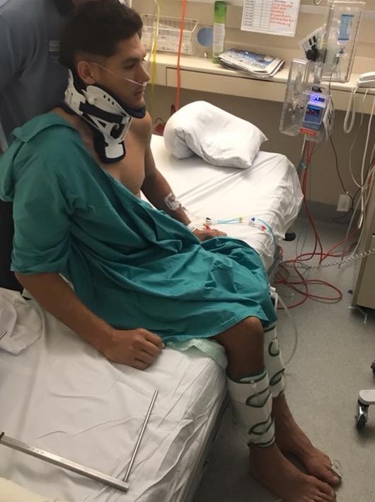 Tai Martin-Page sits on the edge of a hospital bed with his legs and neck in braces.