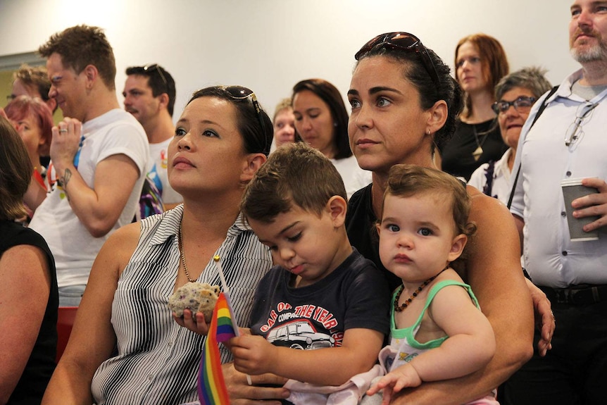 May Dunlop and Lisa Menchetti hold their toddlers in a crowded room.