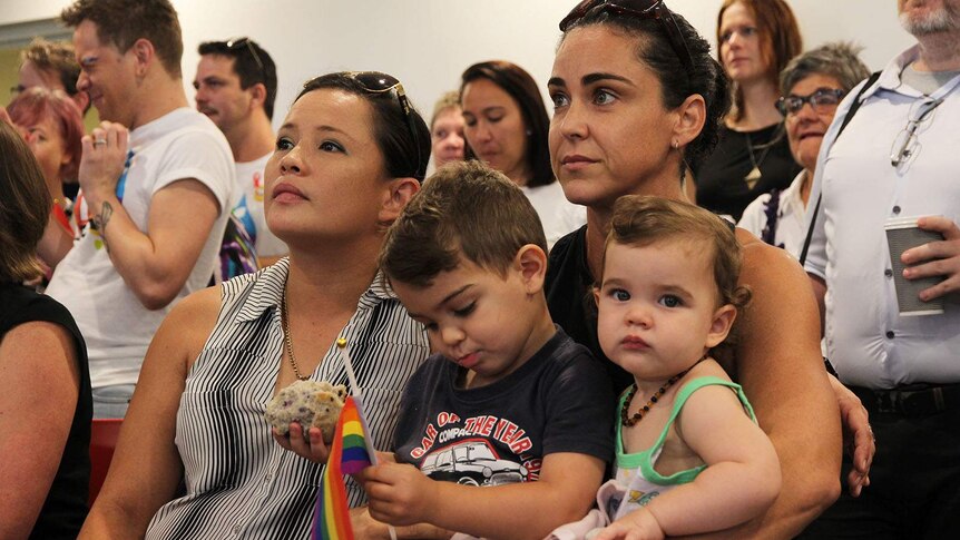 May Dunlop and Lisa Menchetti hold their toddlers in a crowded room.