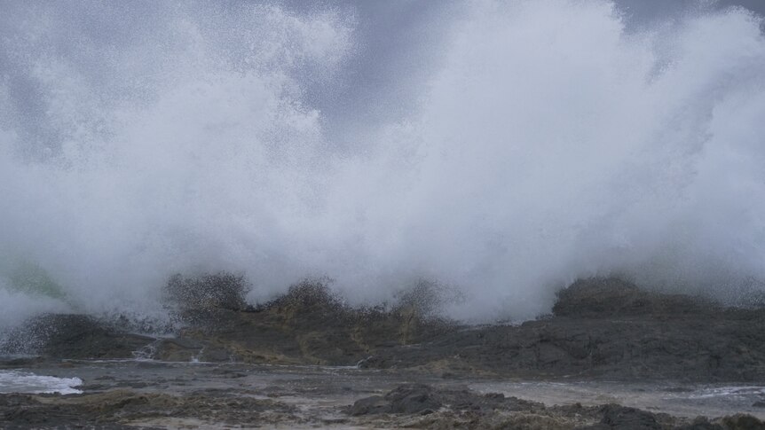 Sea water turns to spray as it smashes into rocks.