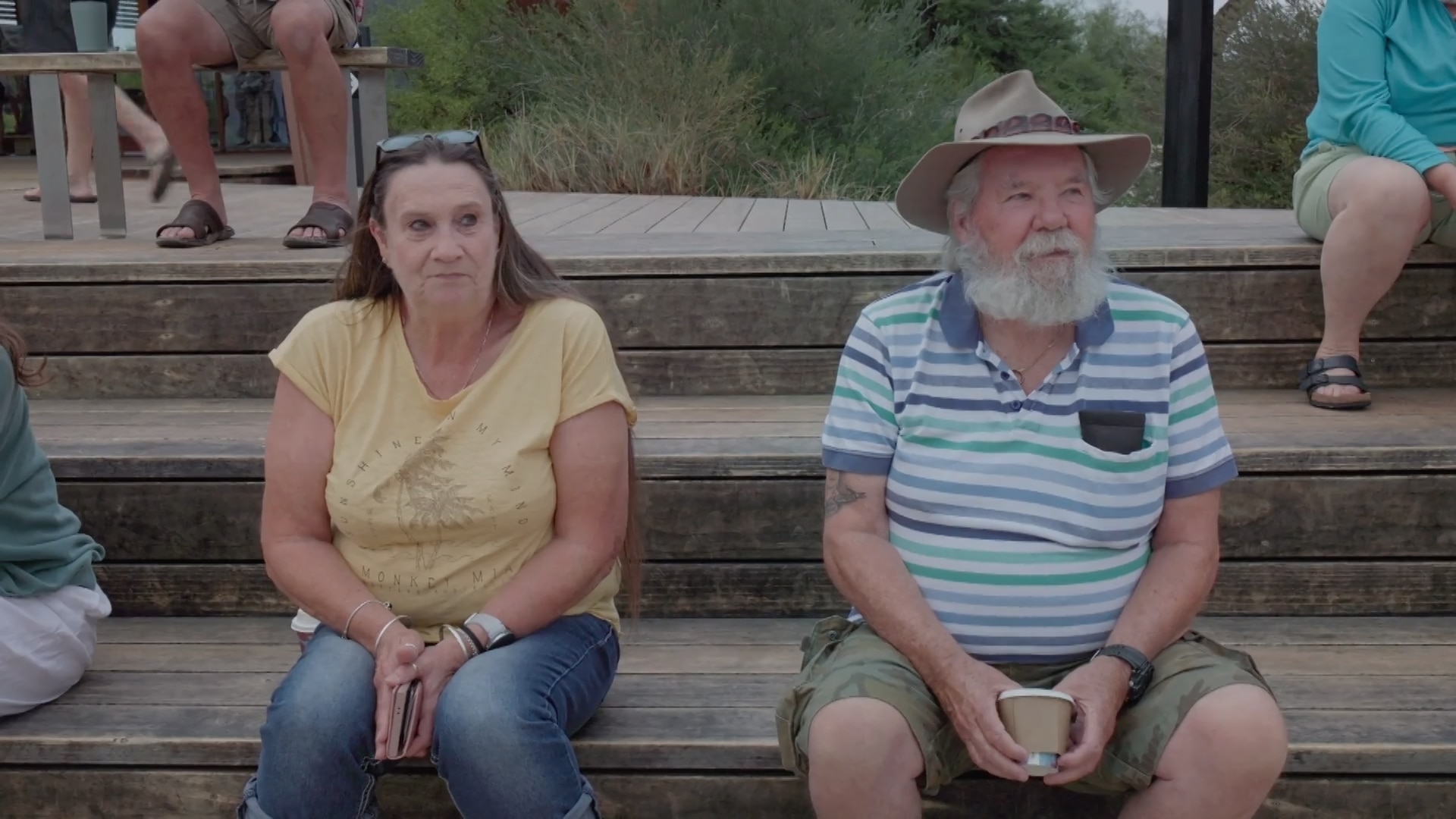 Una mujer y su marido se sientan expectantes sobre unos escalones de madera.