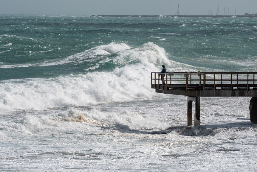 A photo of a man standing on a jetty in front of a rough ocean.
