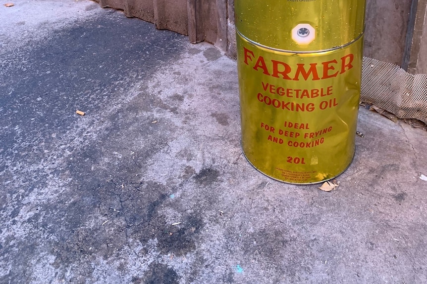 A gold oil barrel next to a fence on stained pavers
