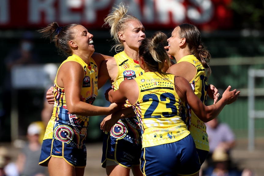 Four Adelaide Crows AFLW players embrace as they celebrate a goal against Collingwood.
