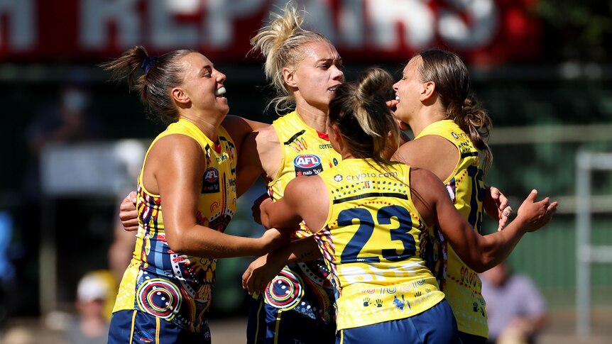 Four Adelaide Crows AFLW players embrace as they celebrate a goal against Collingwood.