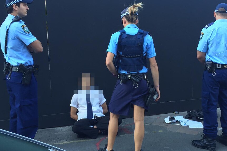 Student sits on the ground outside Arthur Phillip High in Sydney while surrounded by police.