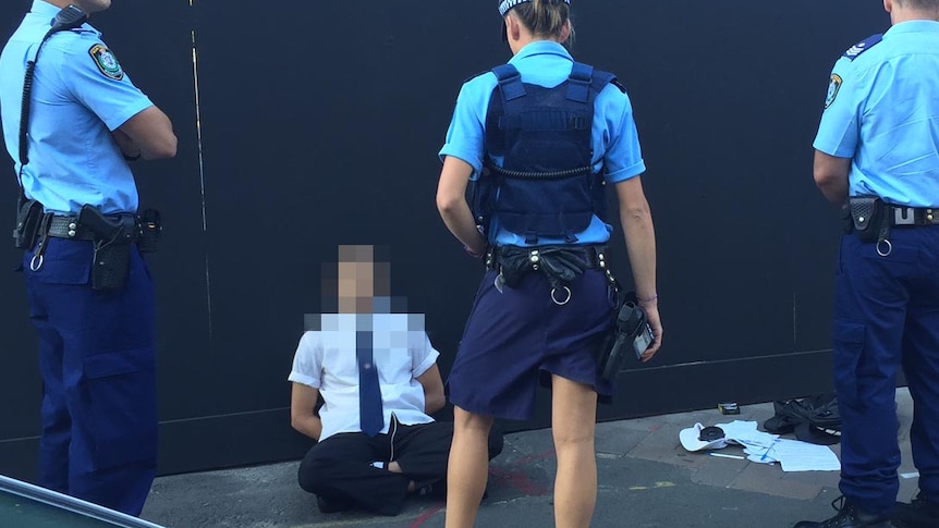 Student sits on the ground outside Arthur Phillip High in Sydney while surrounded by police.