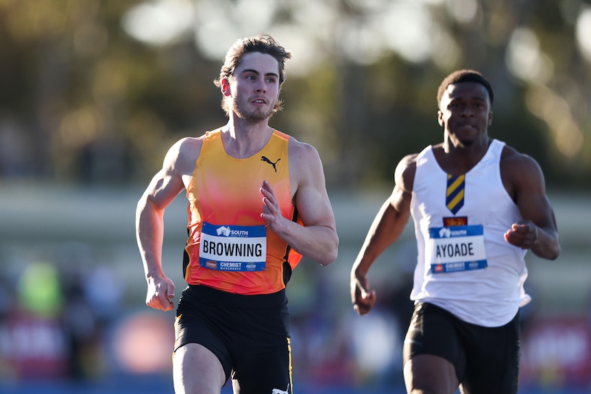 Two Australian men's athletes finish a 100m race, with the winner (left) looking to his right. 