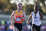 Two Australian men's athletes finish a 100m race, with the winner (left) looking to his right. 