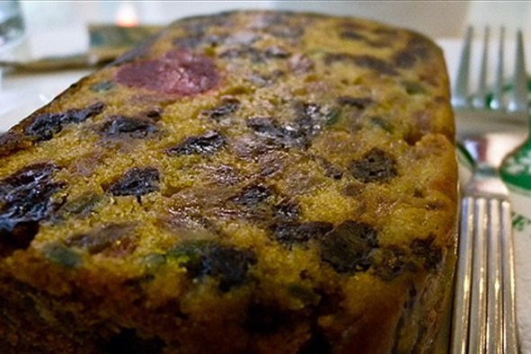 A slice of fruit cake on a plate with a fork beside it.