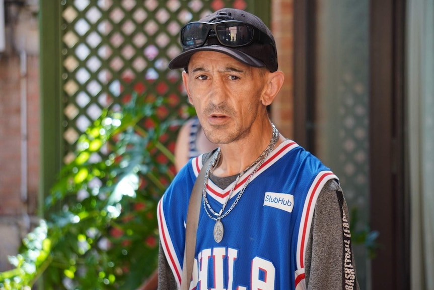 A man wearing a basketball jersey and black cap poses for a photo.