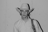 A black and white portrait of a young man in a cowboy outfit.