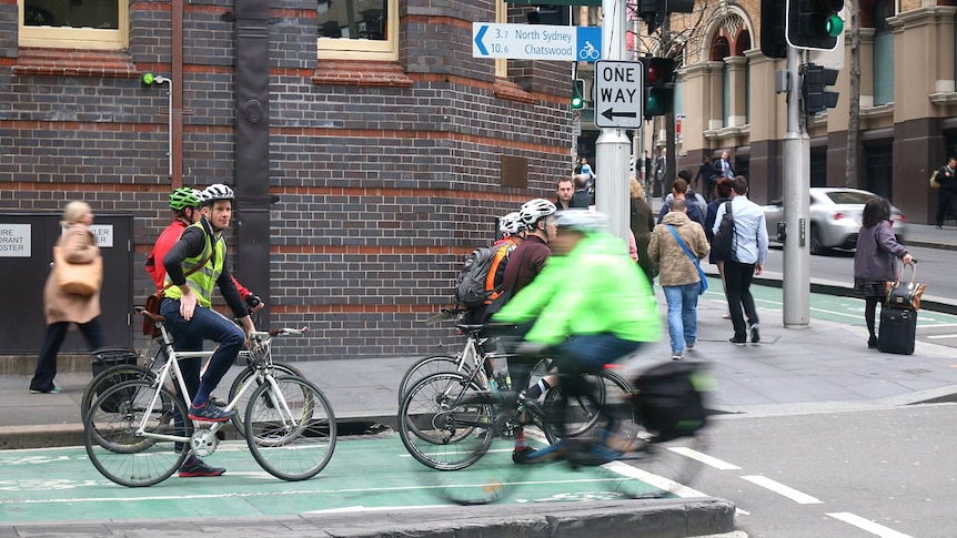 People sitting on bicycles at an intersection with traffic lights.