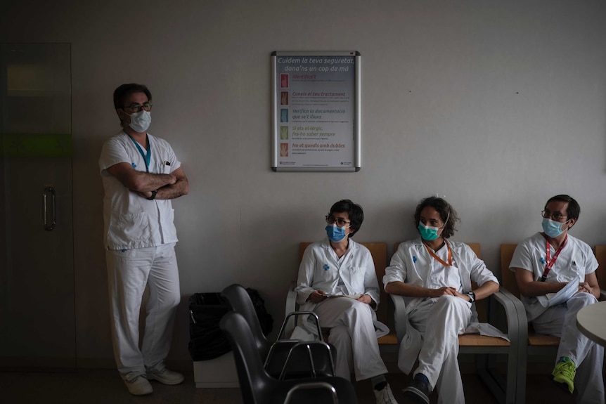 Four workers in white scrubs lean against a wall