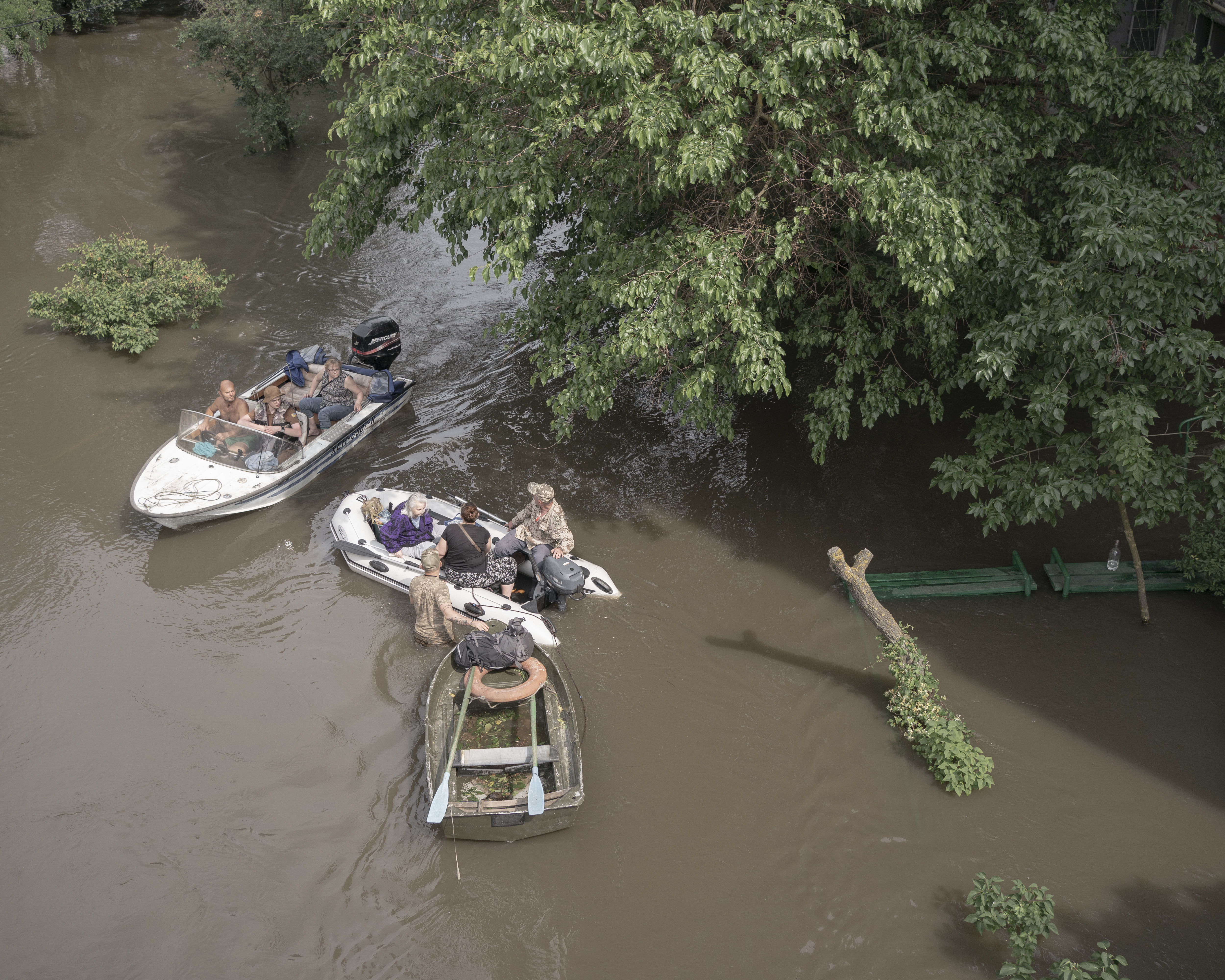People gather together in three small boats in a flooded tree-filled area