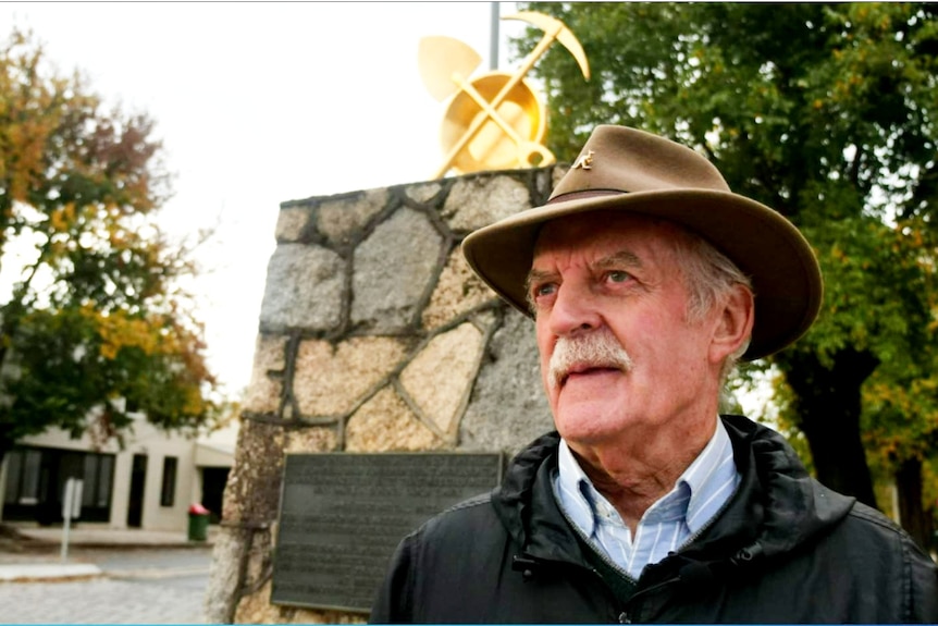 A man looks into the distance with historic gold mining equipment behind him