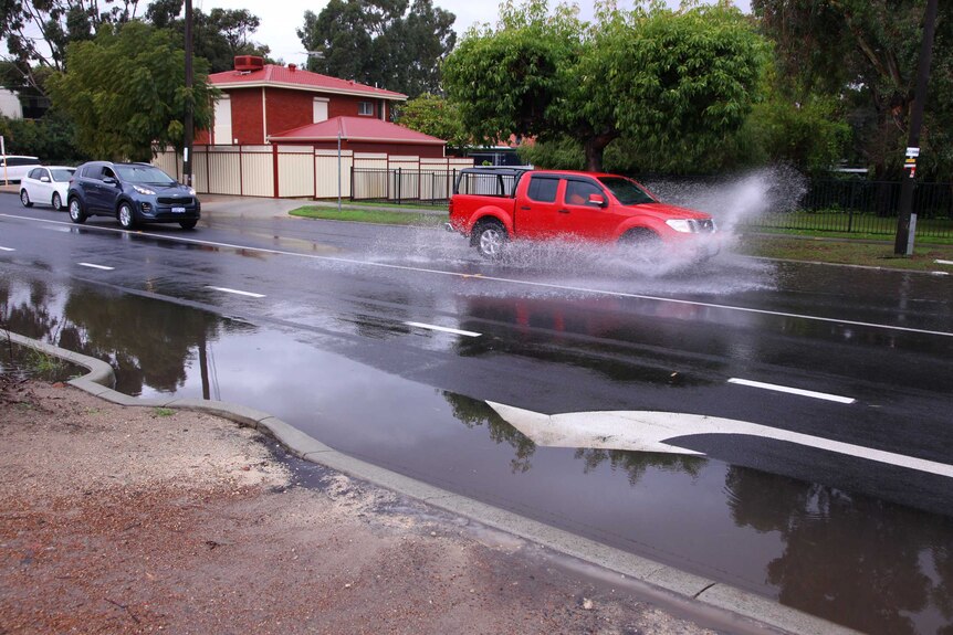A utility splashes water as it drives through a large puddle on a wet August day in Perth.