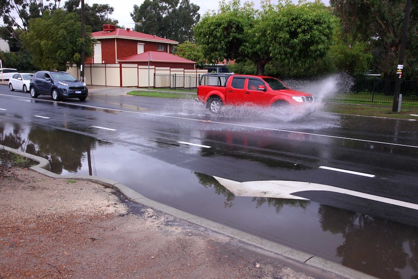 A utility splashes water as it drives through a large puddle on a wet August day in Perth.