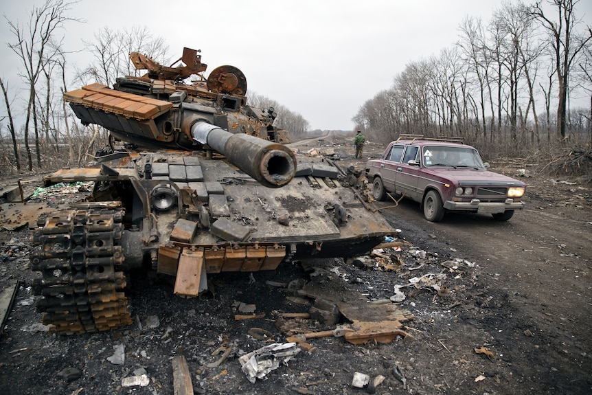 A car passes a destroyed tank abandoned on the road