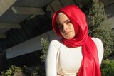 Sara Awamleh poses for a photo sitting outside with a red hijab on.