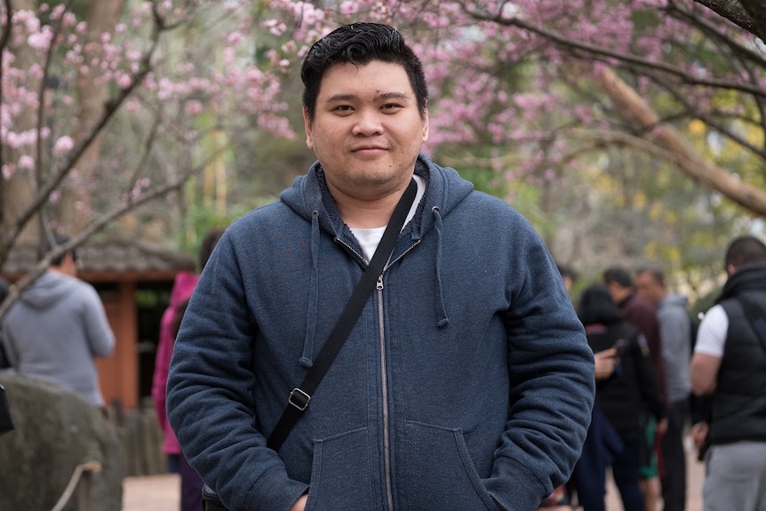 Brendan Vo is standing in a cherry blossom garden.