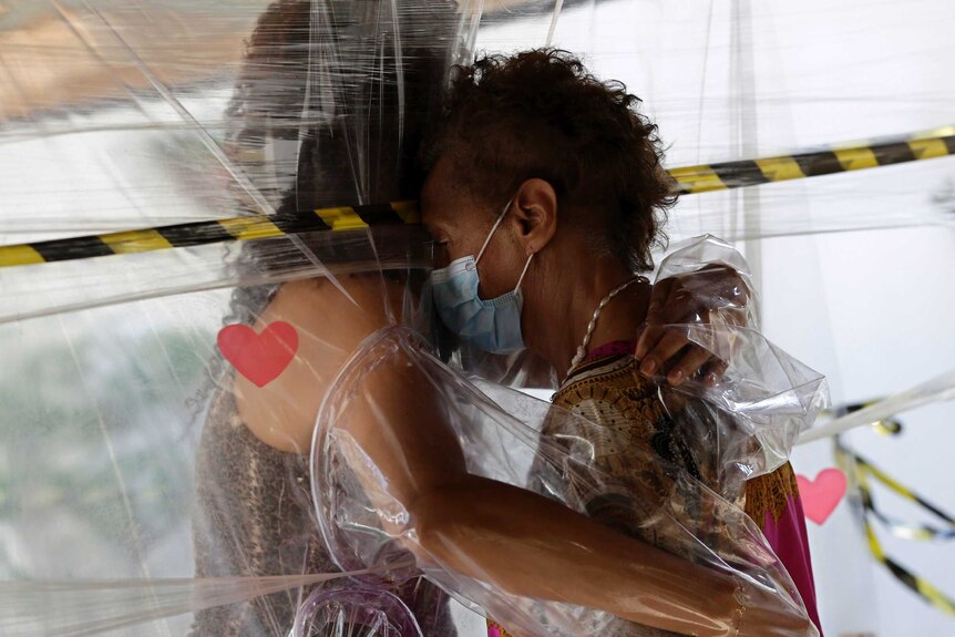 An elderly woman hugs her niece through a plastic barrier during a visit to a retirement home.