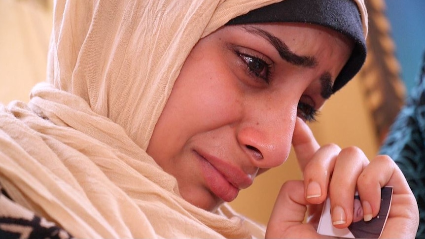 A young woman wipes away a tear while holding a photo of her mother.